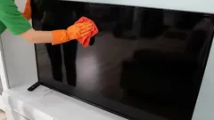 Čistenie obrazovky televízora oranžovou handričkou a rukavicami doma.