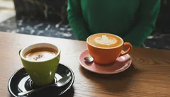 Dve šálky kávy na stole, jedna s latte art, druhá s obyčajnou kávou, kaviareň.