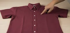 Červená košeľa s krátkym rukávom položená na stole, ruka ukazuje na prednú časť.