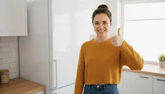 Usmiata žena v kuchyni ukazuje palec hore na znak spokojnosti
